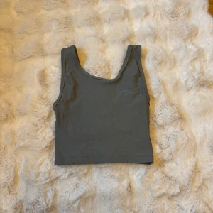 Grå croppad linnetopp från Bik Bok - Säljer en stilren grå croppad linnetopp från Bik Bok i storlek XS. Toppen är ärmlös med breda axelband och har en enkel, clean design som passar perfekt till jeans eller kjol. Tillverkad i mjuk och stretchig bomullsmix för en bekväm passform.