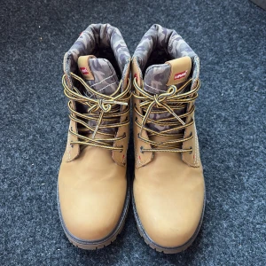 Levi's camelbruna boots med camo-detalj - Säljer ett par Levi's boots i camelbrunt skinn med grov sula och snörning. Skaftet har en snygg camouflagemönstrad vaddering och klassiska Levi's-detaljer. Perfekta för dig som vill ha en robust och stilren look med streetkänsla. Kostar 100kr extra om man vill frakta. Så om man vill frakta bör man betala 800, pris kan diskuteras.