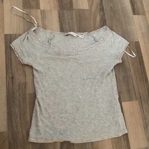 Ljusgrå offshoulder topp med spets - Säljer en ljusgrå offshoulder topp från 157 i storlek XS. Toppen har korta ärmar och fina spetsdetaljer längs halsringningen och ärmsluten. Den är tillverkad i mjuk bomull och har smala axelband för extra support. Perfekt för en chill och söt look.