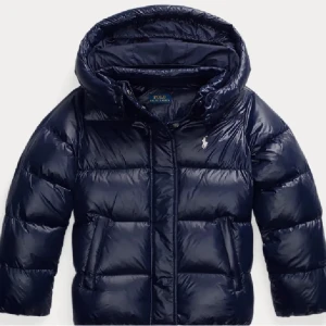 Mörkblå dunjacka Polo Ralph Lauren xs/s - Snygg mörkblå dunjacka från Polo Ralph Lauren i storlek XL (155-159cm). Jackan har en glansig finish, huva och klassisk logga på bröstet. Perfekt för kalla dagar med sin quiltade design och dragkedja framtill. Jackan är i fint skick och passar dig som har storleken xs/s! Orginalpris: 3295kr 