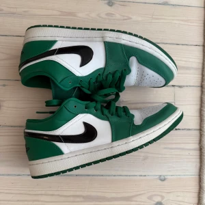Nike Air Jordan 1 Low Pine Green - Säljer ett par Nike Air Jordan 1 Low i fräscha färger – vitt och grönt med svarta swoosh-detaljer. Klassisk siluett med snörning, rund tå och platt sula. Skorna är i skinn och har den ikoniska Air Jordan-loggan på hälen. Perfekta för dig som vill sticka ut med stil. Mycket bra skick, köpt i Kanada, kan skickas eller hämtas :)