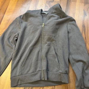 Grå hoodie med dragkedja från 157 - Mörkgrå hoodie från 157 i storlek S. Tröjan har hel dragkedja framtill, huva och en stor känguruficka. Tillverkad i mjuk bomullsmix och har långa ärmar med ribbade muddar. Perfekt för chill dagar eller när du vill vara extra bekväm.