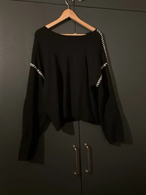 Svart stickad tröja med vita detaljer - Säljer en svart stickad tröja från Y.A.S med vita ränder längs axlar och ärmar. Tröjan har en loose passform och långa ärmar, perfekt för dig som gillar en avslappnad stil. Snygg men bekväm tröja!