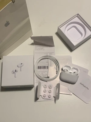 AirPods Pro (2nd Generation) - Apple AirPods Pro (2nd Generation) i mycket fint skick, komplett med originalförpackning, laddningskabel, extra öronproppar och kvitto. Allt ser ut att vara i nyskick utan synligt slitage. Perfekt för dig som vill ha trådlösa hörlurar med aktiv brusreducering.