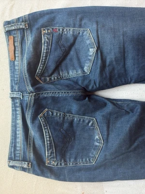 Blå bootcut jeans från Replay Rockxanne - Säljer ett par snygga blå jeans från Replay, modellen Rockxanne. Jeansen har bootcut passform, låg midja och klassiska fem fickor. Materialet är mjukt jeans med lätt slitningar och detaljerade sömmar på bakfickorna. Har sytt både sytt in dem vid låren för att göra dem mer lågmidjade samt för bättre passform, dessutom gjort dem bootcut. Passar 34 och 36, stretchigt material. 