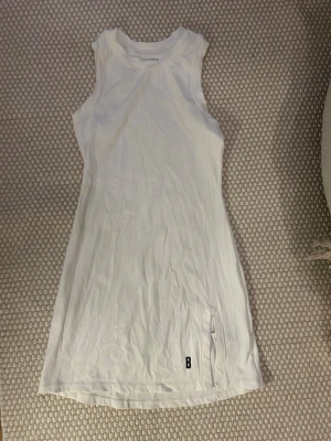 Helt ny! Vit sport klänning från Björn Borg - Säljer en vit, ärmlös kort klänning från Björn Borg. Klänningen har en tight passform, rund halsringning och liten slits med ett B-tryck nertill. Tillverkad i mjuk och stretchig bomullsmix, perfekt för en varm sommardag på tennisplanen