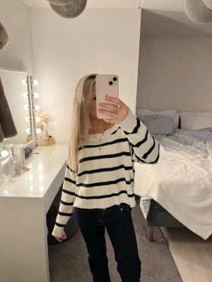 Randig stickad tröja i vitt och svart - Säljer en mysig stickad tröja med svarta ränder på vit botten. Tröjan har en avslappnad passform, långa ärmar och ribbade muddar. Perfekt att slänga på sig för en chill look.