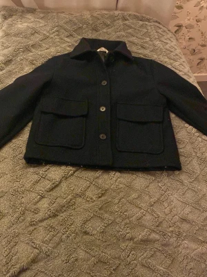Marinblå kappa från H&M, strl 152 - Stilren svart overshirt från H&M i storlek 152. Jackan har klassisk krage, stora framfickor och knäppning med knappar. Perfekt för dig som gillar enkel och clean look. Materialet känns mjukt och lite tjockare, perfekt för lager på lager.