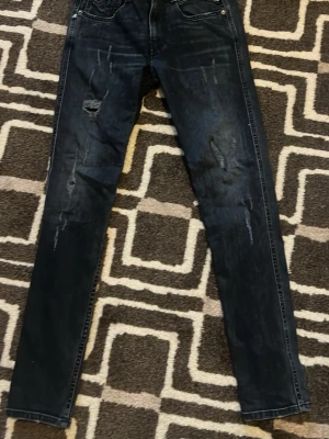 Mörkablå Replay jeans slitningar - Säljer ett par mörkblå slim jeans från Replay med slitna detaljer och distressed look på framsidan. Jeansen har klassisk femficksdesign och smal passform hela vägen ner. Perfekta för dig som gillar en trendig stil. Storlek 28 30