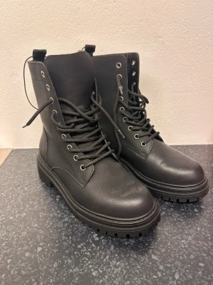 Svarta boots med snörning och foder - Säljer ett par chunky svarta boots med snörning och grov sula. Skorna är fodrade med mjukt material på insidan och har rund tå. Helt nya.