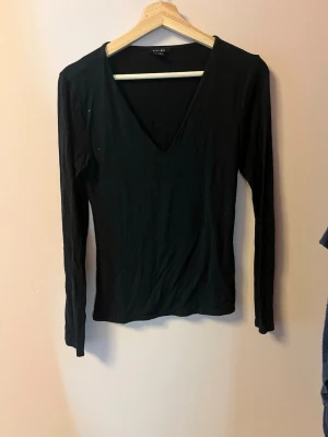 Svart långärmad topp från Amisu - En svart långärmad topp från Amisu med djup v-ringning. Toppen har en enkel och stilren design i mjukt material som sitter nära kroppen. Perfekt att matcha med jeans eller kjol för en clean look.