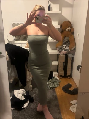 Grön ribbad axelbandslös långklänning - Säljer en snygg grön axelbandslös långklänning i ribbat material. Klänningen är tight och har en slits bak som gör den extra bekväm och stilren. Perfekt för dig som gillar en enkel men trendig look.