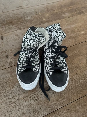 Converse sneakers med textmönster - Säljer ett par Converse sneakers med svart och vitt textmönster där det står 'MY STORY'. Skorna har svart tå, vita tjocka platåsulor och svarta skosnören. Klassisk rund tå och högt skaft. Perfekta för dig som vill sticka ut med coola detaljer.
