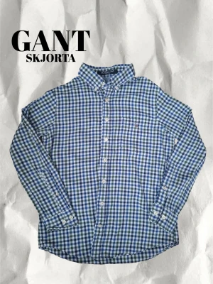 GANT Skjorta - Vi säljer en snygg rutig Gant skjorta. Skjortan har en bröstficka med en liten fläck på den, men denna fläck syns knappt, (se bild). Annars är skjortan helt felfri. Skjortan är i storlek 134-140cm. Checka in vårat konto för ännu stiligare produkter och skriv gärna om ni har fler frågor eller vill ha bilder!