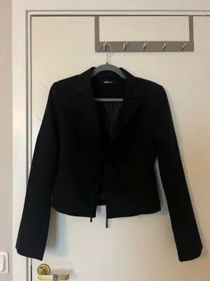 Svart kavaj - Säljer denna kavaj med knytning fram från Gina Tricot, detta då den inte används längre. Kavajen är figursydd. Nypris är 499kr men säljer för 200kr, pris kan diskuteras. 