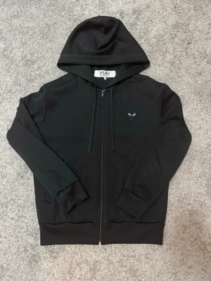 Comme des Garcons Hoodie - Mycket bra skick använd ett par gånger. Den ända defekten som finns är ett litet hål på hjärtat där bak som man kan se på bild 2, men man märker knappt annars är den fin. Sitter som storlek M i bredden men kortare i längden. DM för mer info och referens med bilder ℹ️