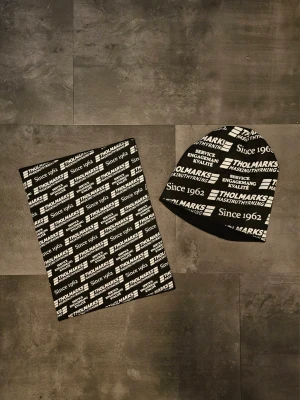 Mössa och halsvärmare  - Säljer ett set med svart och vit mössa och matchande halsvärmare från Tholmarks. Båda plaggen har ett tryckt logomönster med texten 'Since 1962". Tillverkade i mjuk polyester som passar perfekt för kyliga dagar.