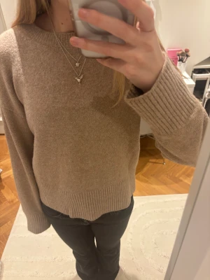 Beige stickad tröja - Säljer en beige stickad tröja med rund hals och breda ribbade muddar vid ärmslut och nederkant. Tröjan har en enkel och clean look, perfekt för dig som gillar neutrala färger och mjuka material. Passformen är normal och ärmarna är långa.
