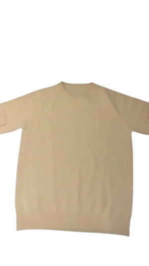 Beige stickad tröja med rund hals - En stilren beige stickad tröja med rundad hals och ribbade muddar vid ärmslut och nederkant. Tröjan har en klassisk, enkel design och är långärmad, perfekt för dig som gillar neutrala färger och mjuka material. Har aldrig använt denna tröjan