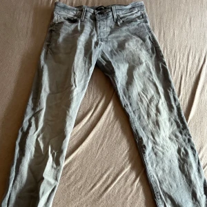 Grå slim jeans från Jack & Jones - Slim fit jeans från Jack & Jones i en snygg ljusgrå tvätt. Klassisk femficksmodell med dragkedjegylf och bälteshällor. Jeansen är tillverkade i bomull med en smal passform som sitter snyggt längs benen.