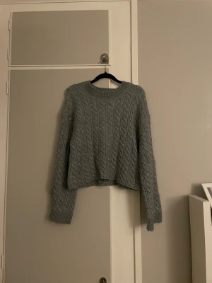 Grå stickad tröja från Lindex - Säljer en grå stickad tröja från Lindex i storlek S. Tröjan har ett snyggt flätmönster, rund hals och långa ärmar med ribbade muddar.🩷