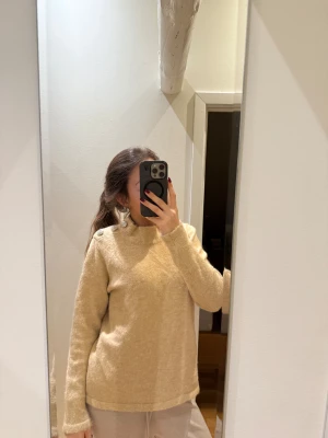 Beige stickad tröja med glittriga knappar - Supermysig beige stickad tröja med rund hals och tre stora glittriga knappar på ena axeln. Tröjan är från Massimo Dutti och är använd ca 3 gånger. Det sticks ej. 