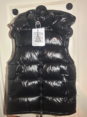Moncler väst  - Snygg och modern Moncler-väst i svart – klassiker som aldrig går ur tiden. Helt ny och oanvänd! Lätt, bekväm och perfekt lager-på-lager året runt. Passar lika bra över hoodie som tröja för en premium look.  ✔ Storlek: M ✔ Skick: Helt ny ✔ Färg: Svart  Ett måste för alla Moncler-älskare 🤩 