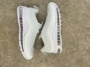 Nike Air Max 97 Triple White - Säljer ett par Nike Air Max 97 i helvitt. Skorna har den ikoniska vågiga designen, synlig Air Max-sula och snörning. Ovandelen är i syntet och mesh för en clean look. Perfekta för dig som gillar stilrena sneakers med futuristisk vibe.