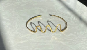 Guldigt vågigt armband i metall - Unikt armband i guldig mässing med vågig design framtill. Öppen modell som enkelt träs på handleden och ger en cool, modern vibe. Perfekt för dig som gillar statement-smycken och vill sticka ut med något annorlunda.