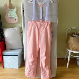 Ljusrosa skidbyxor - Fina ljusrosa täckbyxor/skidbyxor med vita hängslen. Byxorna har raka ben och knäppning fram med knapp och dragkedja. 💖 Köptes förra säsongen men användes aldrig för dom var lite för små för mig som har midja 74cm och höft 104cm. Skulle uppskatta storlek 36 eller S! Supervarma och mysiga, man syns verkligen i backen med dessa 💖💖