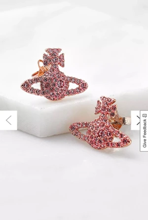 Vivienne Westwood rosa örhängen - Säljer ett par ikoniska Vivienne Westwood örhängen i planetform, täckta med rosa glittrande stenar. De har en cool och unik design med små kristaller som ger extra bling. Perfekta för dig som vill sticka ut med ett statement-smycke.
