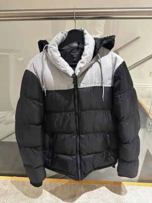 Svart och vit pufferjacka Project X Paris - Säljer en snygg pufferjacka från Project X Paris i storlek S men passar också som en storlek M. Jackan är svart med grå panel upptill, justerbar luva med snörning och dragkedja framtill. Fodret är mjukt och jackan har två sidofickor med dragkedja. Perfekt för kalla dagar och streetwear-stil. Skriv efter minsta lilla fundering!! Pris kan diskuteras!!