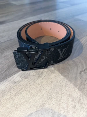 Svart Louis Vuitton bälte i skinn - Säljer ett svart Louis Vuitton bälte i skinn med klassiskt monogrammönster i grått och en stilren LV-spänne i svart metall. Bältet har en bred och rak form som ger en lyxig vibe och passar perfekt till jeans eller kostymbyxor. Kan sänka priset vid snabb affär. snabb frakt 