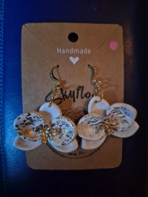 Handgjorda blommiga örhängen Skyflora - Unika handgjorda örhängen från kanadensiska Skyflora i form av vita blommor med guldiga detaljer och stänk. Hängande modell med guldfärgade krokar, perfekt för dig som vill sticka ut med ett kreativt och konstnärligt smycke.