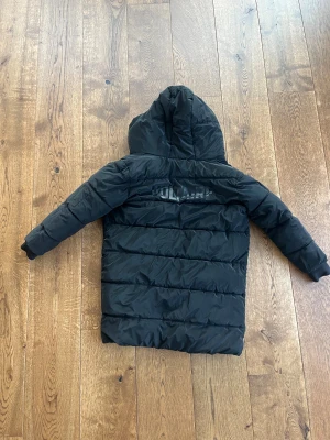 Vändbar vinterjacka från Zadig & Voltaire - Knappt använd, vändbar varm och lång pufferjacka från Zadig & Voltaire med huva. Ena sidan är svart med diskret logga på ryggen, andra sidan är olivgrön med broderad vinge på ärmen. Jackan har dragkedja, fickor och quiltad design. Perfekt för kalla dagar och snygg att bära oavsett stil.