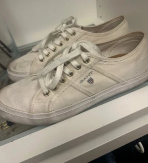 Vita sneakers från Gant - Snygga vita sneakers från Gant med klassisk låg profil och rund tå. Skorna har snörning med metallöglor och är tillverkade i bomullstyg med Gant-logga på sidan. Perfekta för en clean och avslappnad stil.