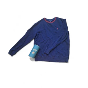 Blå långärmad tröja från Polo Ralph Lauren - Snygg marinblå långärmad tröja från Polo Ralph Lauren med röd broderad logga på bröstet och kontrastfärgade röda sömmar vid halsen. Tröjan har rund hals och är gjord i mjuk bomull, perfekt för chill dagar.