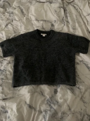 Mörkgrå croppad stickad tröja - Mysig mörkgrå stickad tröja med korta ärmar och croppad passform. Perfekt för lager-på-lager och chill dagar. Rund halsringning och mjukt material som känns skönt mot huden.