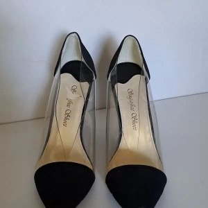 Svarta transparenta wedges med spetsig tå - Snygga wedges med svart mocka på tå och häl, transparent plast längs sidorna och spetsig tå. Klacken är hög och kilformad, vilket ger extra höjd och stabilitet. Insidan är ljusbeige med logotyp. Perfekt för dig som gillar statement-skor med modern vibe.