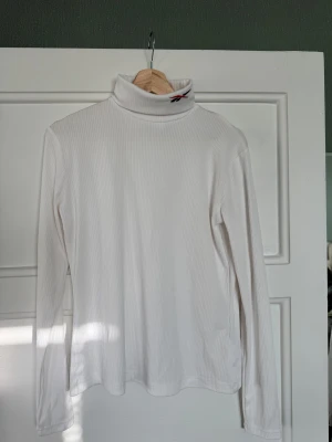 Vit ribbad polotröja från Reebok - Vit ribbad polotröja från Reebok med broderad logga på kragen och i nacken. Tröjan har lång ärm och är i mjukt, stretchigt material som sitter snyggt. Perfekt att styla med jeans eller kjol för en clean look.
