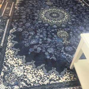 Mattor  - Vardagsrumsmattan: Den stora vardagsrumsmattan har ett elegant och harmoniskt mönster i djupa blå toner som ger rummet en lugn och exklusiv känsla. Det centrala medaljongmönstret skapar en vacker fokuspunkt och de ljusare detaljerna runt kanterna ger mattan liv utan att ta över. Den binder ihop inredningen på ett väldigt stilfullt sätt och gör rummet både ombonat och sofistikerat.  Hallmattan: Hallmattan är lång, stilren och perfekt proportionerad för att möta dig direkt när du kommer in. Det mö