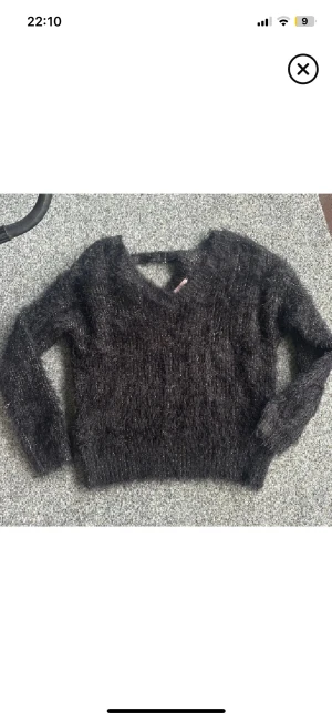 Svart fluffig stickad tröja Sincerely Loved - Mysig svart stickad tröja från Sincerely Loved i storlek S. Tröjan har en fluffig textur med glittriga inslag, v-ringad hals och långa ärmar. Perfekt för dig som gillar en lite loose och comfy stil med extra glans.