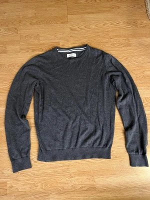  Pier One sweatshirt  - Mörkgrå stickad sweatshirt från Pier One med rund hals och ribbade muddar vid ärmslut och nederkant. Enkel och stilren design som funkar till många olika looks. Materialet är mjukt och skönt, perfekt för kyligare dagar.