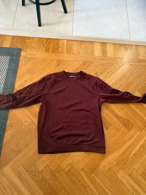 Vinröd sweatshirt från Dressmann XL - Vinröd sweatshirt från Dressmann i storlek XL. Tröjan har rund halsringning med en snygg V-detalj framtill och långa ärmar. Tillverkad i mjuk bomull som är skön mot huden. Perfekt för dig som gillar enkel och stilren design.