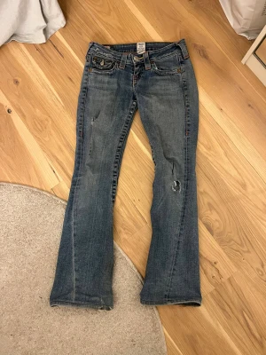 True Religion bootcut jeans - Säljer dessa snygga blåa jeans från True religion med lite slitningar. Knappen på ena bakfickan har ramlat av vilket man kan se på 3 men annars är den i gott skick!