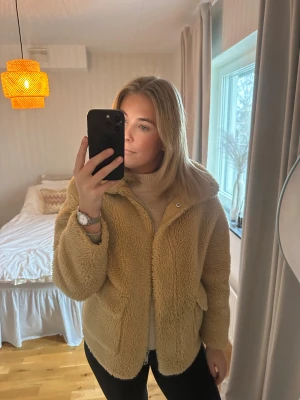 Beige teddyjacka med dragkedja - Mysig beige teddyjacka med stor krage och två rejäla fickor framtill. Jackan har en dragkedja och är tillverkad i fluffigt fleece-material som ger en chill och trendig vibe. Perfekt för att hålla sig varm och se snygg ut under kyliga dagar.
