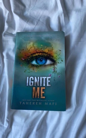 Ignite Me - En bok med ett fängslande omslag som visar ett blått öga omgivet av färgglada blommor och växter. Perfekt för dig som gillar spännande och känsloladdade berättelser. Författaren är en New York Times bestseller, vilket garanterar en gripande läsupplevelse.