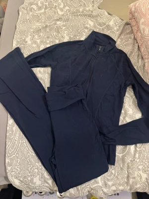 Marinblå träningshoodie och byxor Gina Tricot - Snygg marinblå hoodie och byxor från Gina Tricot med dragkedja framtill och hög krage. Perfekt för träning eller chill, tillverkad i mjuk polyesterblandning. Långärmad och med slim passform som sitter skönt mot kroppen. Matcha med tights för en komplett look.