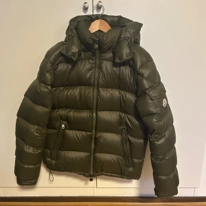 Moncler maya olive  - Säljer denna ÄKTA Moncler maya i färgen Olive matt storlek 3 som motsvarar M/L. Jackan är köpt secondhand på Grailed då det också finns kvitto på detta. Priset är fantastisk på grund av att det är ett litet hål nere vid spännbanden som säkert kan fixas. Vid frågor om jackan eller fler bilder kom pm. 