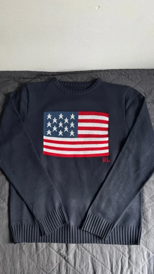 Mörkblå stickad tröja från Ralph Lauren - Mörkblå stickad tröja från Polo Ralph Lauren med USA flagga på framsidan, passformen är slim och storleken är S. Kom dm för mer bilder och frågor !